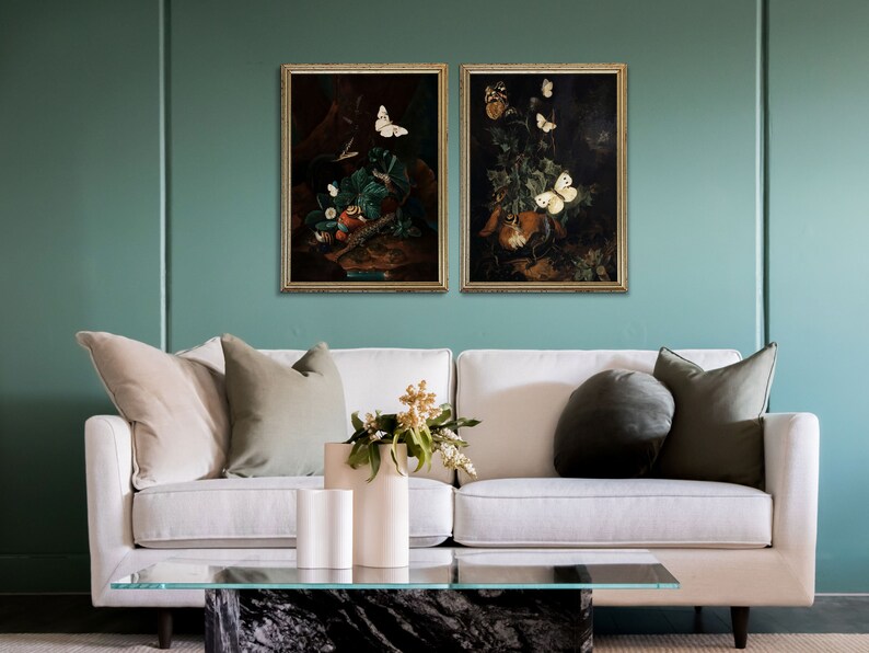 Puede incluir: Dos pinturas enmarcadas de bodegones con mariposas y flores. Las pinturas est&aacute;n en marcos dorados y est&aacute;n colgadas en una pared verde azulada.