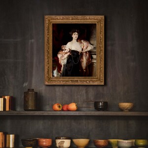 A kitchen with dark walls and open shelves displaying ceramic bowls and a few pieces of fruit. Above the shelves is a framed portrait of a woman in a black and white gown with a red drape, hung on the dark wall.
