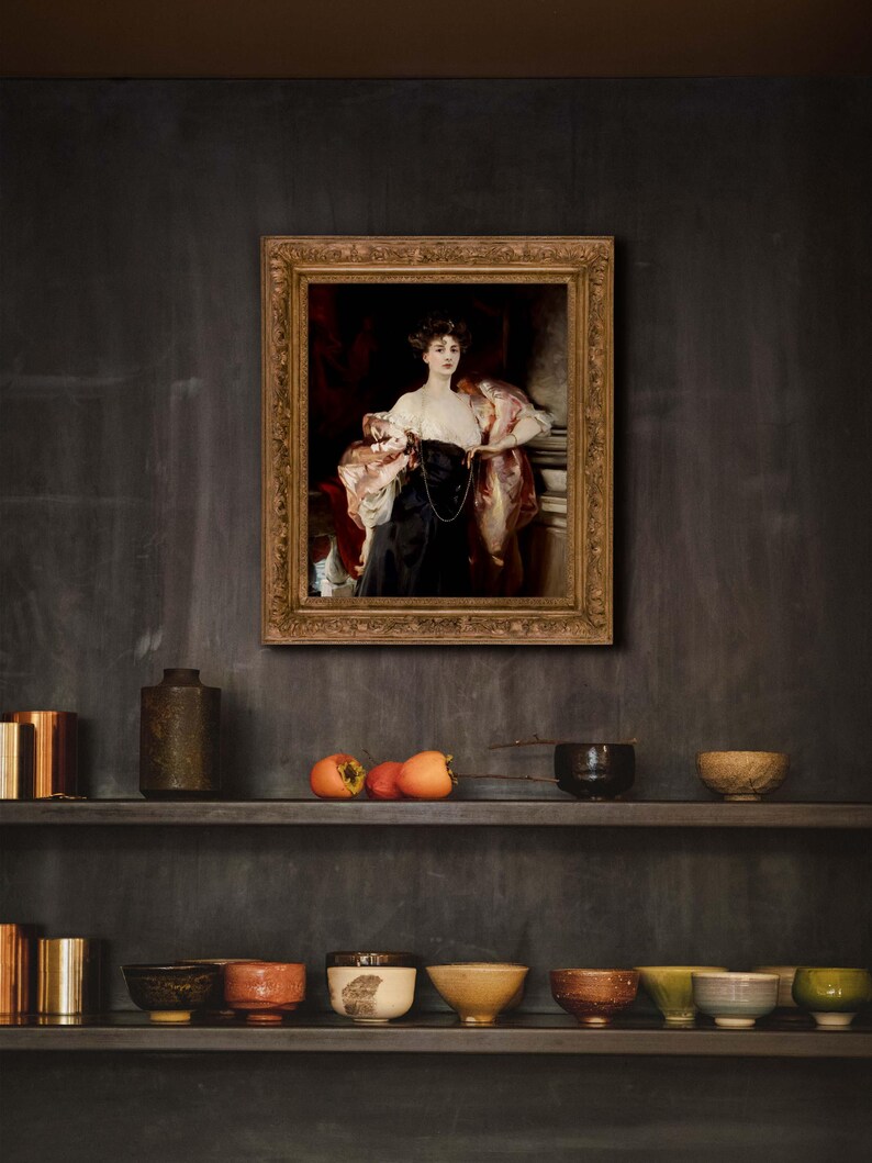 A kitchen with dark walls and open shelves displaying ceramic bowls and a few pieces of fruit. Above the shelves is a framed portrait of a woman in a black and white gown with a red drape, hung on the dark wall.