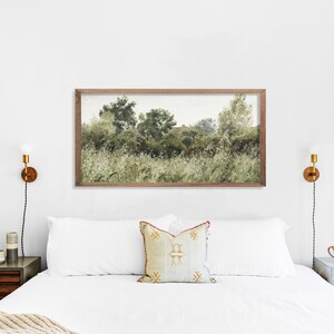 Framed horizontal landscape art print above a white bed, showing wild greenery and softly painted trees with earthy brushstrokes. The neutral tones and minimal color palette create a tranquil Japandi atmosphere with Wabi Sabi elegance, perfect for serene bedrooms.