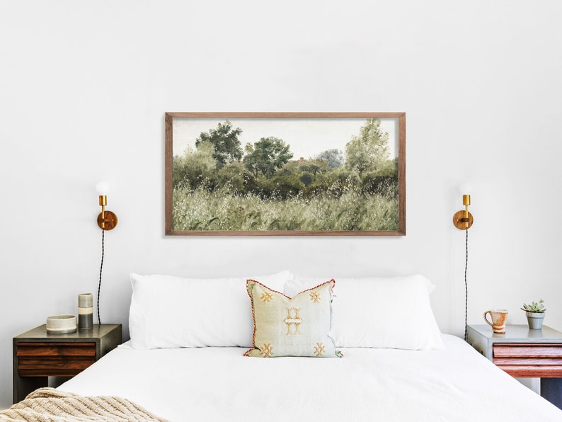 Framed horizontal landscape art print above a white bed, showing wild greenery and softly painted trees with earthy brushstrokes. The neutral tones and minimal color palette create a tranquil Japandi atmosphere with Wabi Sabi elegance, perfect for serene bedrooms.
