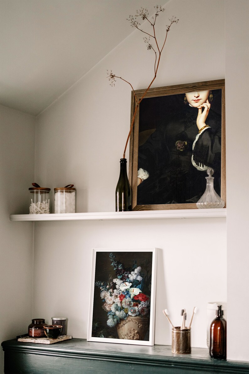 May include: A white shelf with a framed painting of a woman in a black dress, a framed print of a still life with flowers in a vase, two glass jars with lids, a bottle of wine, a glass bottle with a stopper, and two small bowls on a black shelf.
