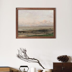 May include: A framed painting of a seascape with a cloudy sky and a distant shoreline. The painting is in a wooden frame and is hanging on a white wall.