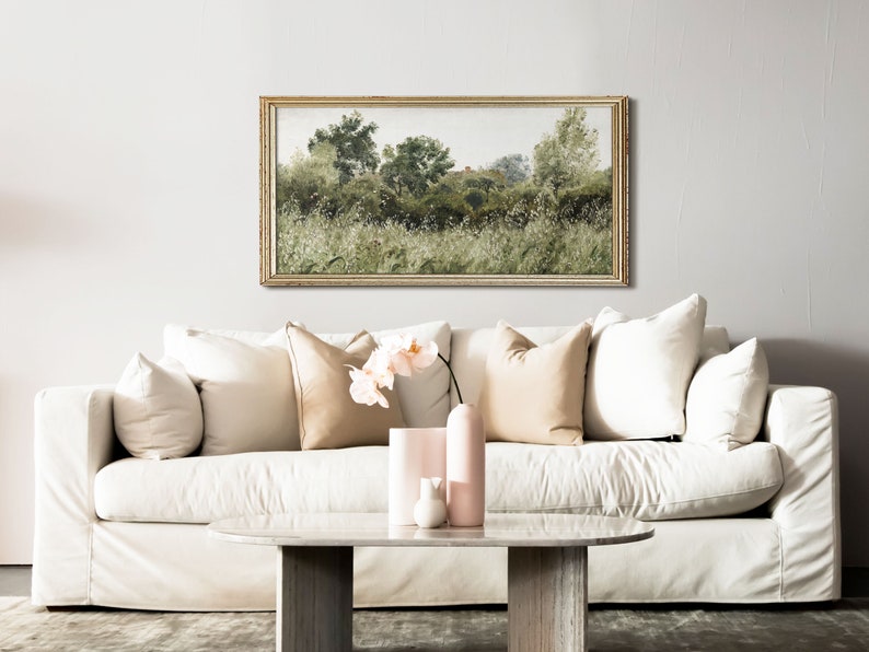 A light-filled living room with a vintage-style botanical landscape framed above a cream sofa. The wild nature scene features earthy greens and soft white highlights, adding Wabi Sabi tranquility and Japandi harmony to a modern organic space.