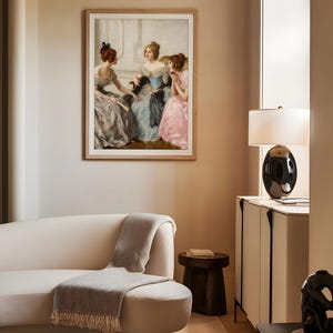 Framed art print of three Victorian women in pastel gowns conversing in an elegant interior, displayed above a curved cream sofa. The soft lighting and muted tones blend classical charm with contemporary living room decor.