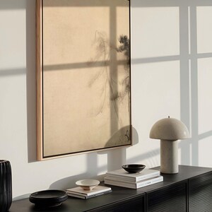Framed wabi-sabi canvas wall art with minimalist pine tree design, styled above a modern black sideboard with ceramic decor and books, in a softly lit interior.