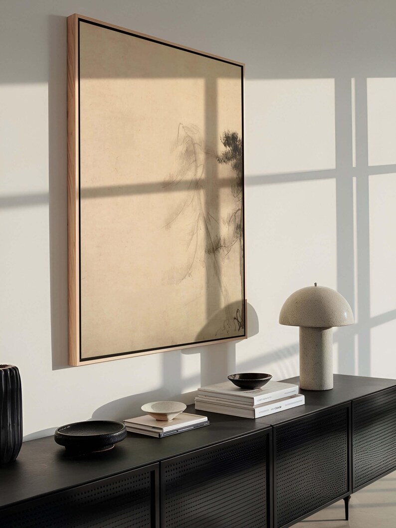 Framed wabi-sabi canvas wall art with minimalist pine tree design, styled above a modern black sideboard with ceramic decor and books, in a softly lit interior.