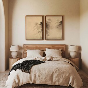 A pair of framed wabi-sabi canvas prints with calming pine tree designs, styled above a neutral bed with soft textiles in a minimalist bedroom featuring wooden furniture and natural tones.