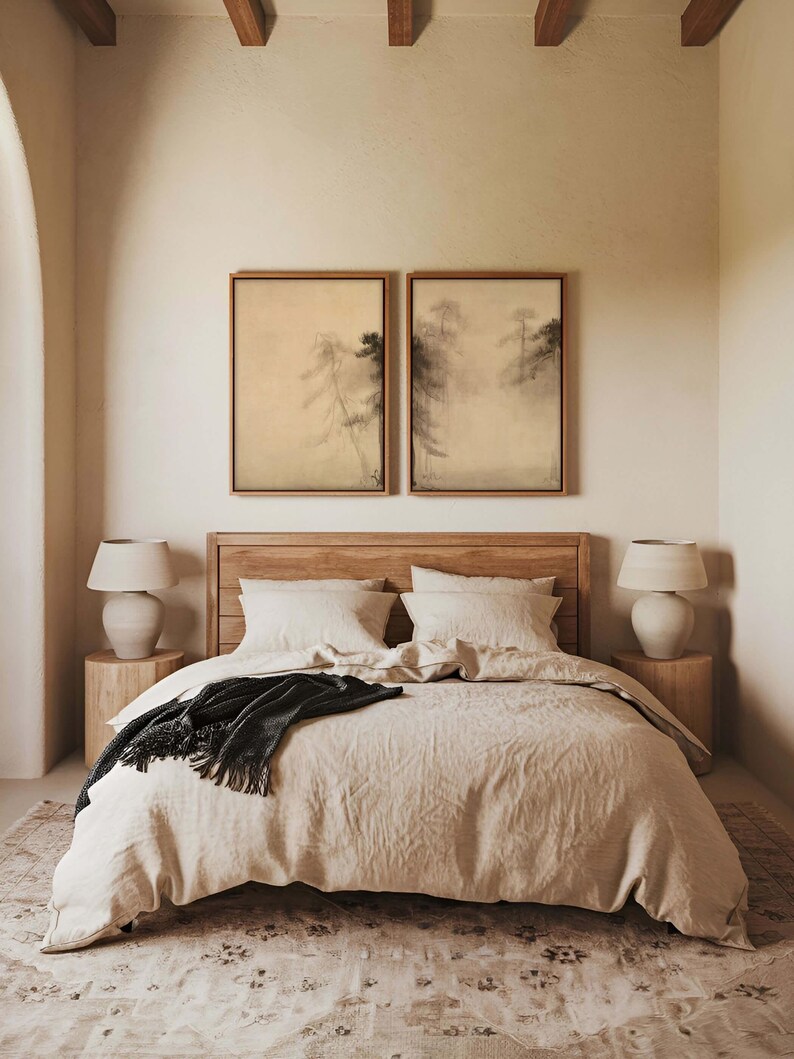A pair of framed wabi-sabi canvas prints with calming pine tree designs, styled above a neutral bed with soft textiles in a minimalist bedroom featuring wooden furniture and natural tones.