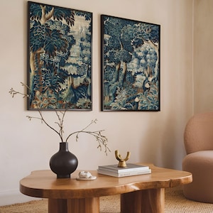 Two framed verdure tapestry prints with deep blue and earthy tones hang above a wooden coffee table in a warm living room. The rich foliage and vintage textile texture create a classic statement wall art set that complements modern decor.