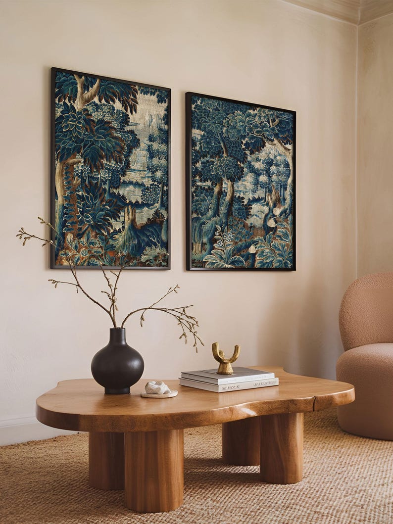 Two framed verdure tapestry prints with deep blue and earthy tones hang above a wooden coffee table in a warm living room. The rich foliage and vintage textile texture create a classic statement wall art set that complements modern decor.