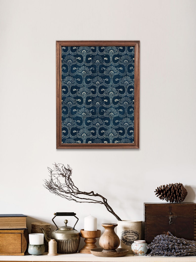 May include: A framed print of a blue and white patterned design. The print is in a wooden frame and is hanging on a white wall. There are various decorative items on a shelf below the print, including a silver teapot, candles, and a wooden vase.