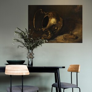 A vintage brass teapot art print is displayed on a sage green wall above a modern black dining table with wooden and gray chairs. A glass vase with greenery adds a fresh touch to the minimalistic, moody interior setting.