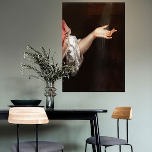 K&ouml;nnte beinhalten: Ein gerahmtes Kunstwerk, das ein klassisches Gem&auml;lde eines Arms zeigt, der nach Wasser greift. Die Person tr&auml;gt einen wei&szlig;en R&uuml;schen&auml;rmel. Das Kunstwerk h&auml;ngt &uuml;ber einem schwarzen Tisch mit zwei St&uuml;hlen.