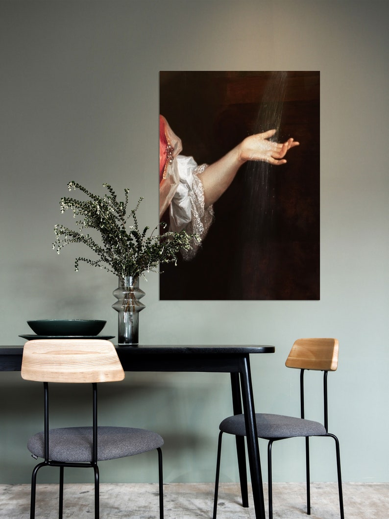 K&ouml;nnte beinhalten: Ein gerahmtes Kunstwerk, das ein klassisches Gem&auml;lde eines Arms zeigt, der nach Wasser greift. Die Person tr&auml;gt einen wei&szlig;en R&uuml;schen&auml;rmel. Das Kunstwerk h&auml;ngt &uuml;ber einem schwarzen Tisch mit zwei St&uuml;hlen.