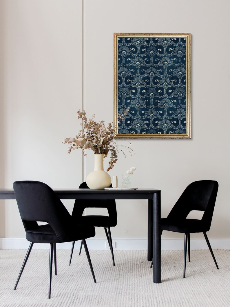 May include: A black and white patterned print in a gold frame hangs above a black dining table with two black velvet chairs. A vase with dried flowers sits on the table.