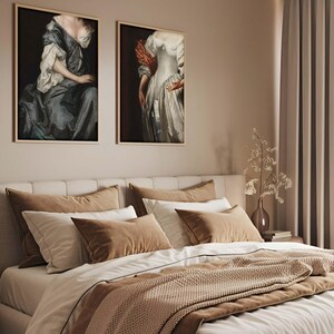 Pair of Baroque portrait prints hanging above a beige and taupe bed with layered textiles. The warm, neutral interior and historical artwork create an inviting, elegant bedroom gallery wall atmosphere.