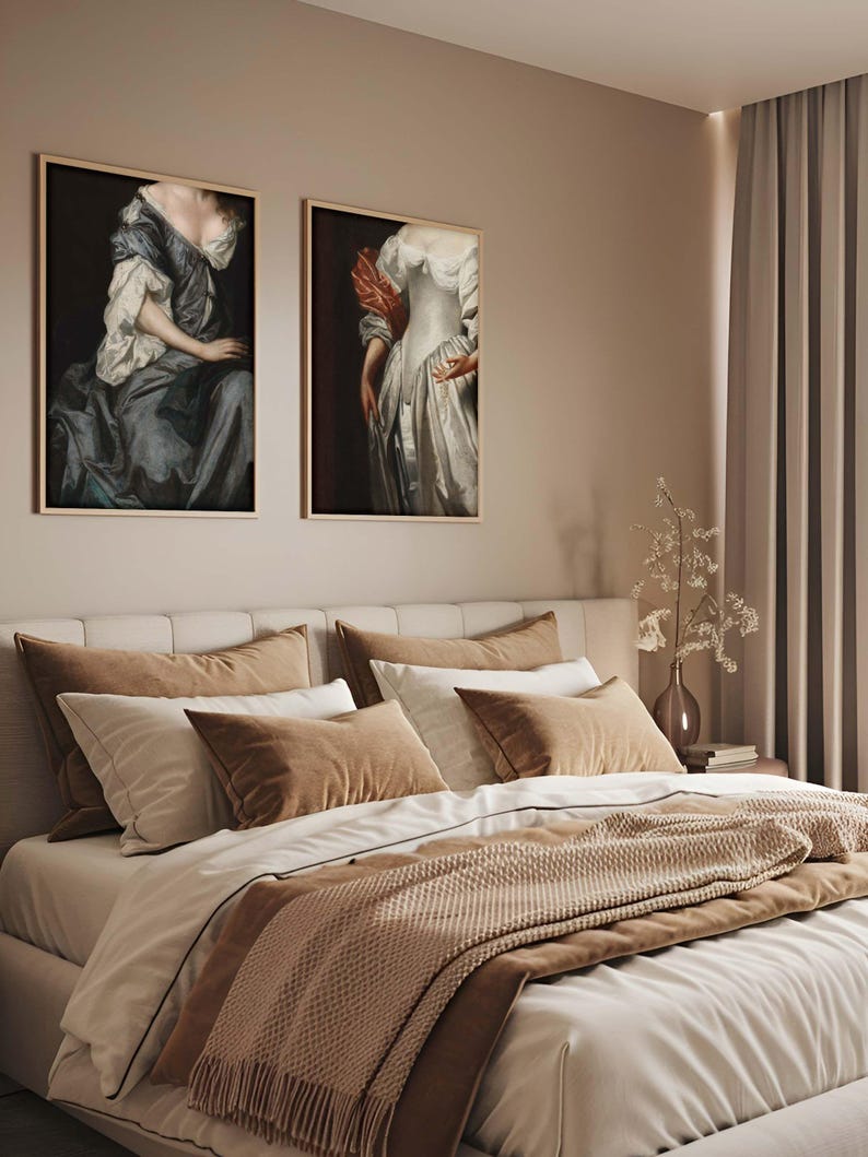 Pair of Baroque portrait prints hanging above a beige and taupe bed with layered textiles. The warm, neutral interior and historical artwork create an inviting, elegant bedroom gallery wall atmosphere.