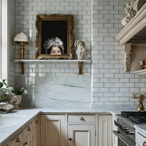 Puede incluir: Una cocina con azulejos blancos, una encimera de m&aacute;rmol y armarios blancos. Un retrato enmarcado de una mujer con un sombrero blanco cuelga sobre la encimera.