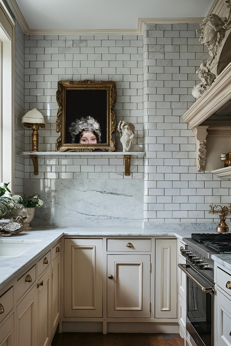 Puede incluir: Una cocina con azulejos blancos, una encimera de m&aacute;rmol y armarios blancos. Un retrato enmarcado de una mujer con un sombrero blanco cuelga sobre la encimera.
