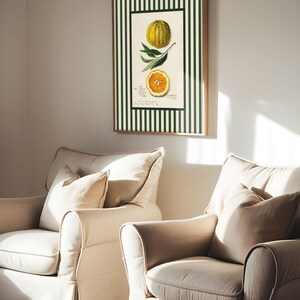 Green-striped orange print in a wooden frame hanging between two beige armchairs in a softly lit living room. A playful blend of traditional botanical and modern cottage aesthetic.