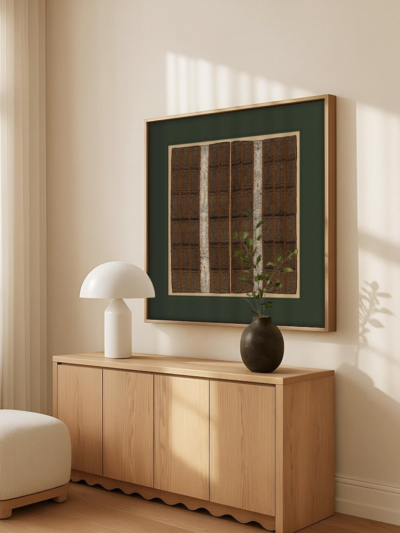 Vintage textile art print with brown woven patterns and green border, displayed above a modern sideboard with neutral decor in a bright living room.