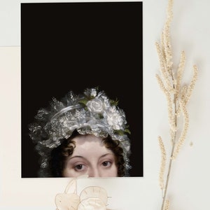 Art print laying on  a white surface. The poster shows the face of a woman at the bottom of it, her head can be seen from the nose up. She is wearing a lace bonnet with white flowers, the background is black.