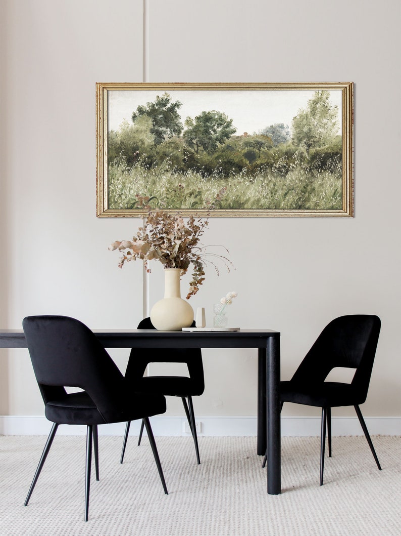 This romantic countryside painting hangs above a modern black dining table with dried florals, combining vintage textures with contemporary Japandi elegance. The soft greenery and subtle aging of the artwork reflect Wabi Sabi beauty and timeless calm.