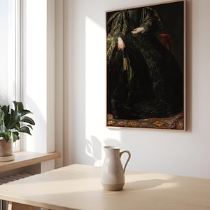 A framed portrait of a woman in a dark, intricate gown is hung on a white wall in a bright dining room. The wooden table below holds a simple ceramic pitcher, with sunlight streaming through the window, illuminating the minimalist modern decor.