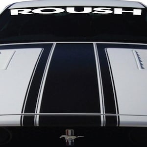 Puede incluir: Coche blanco con franjas negras de carreras en el capó. La palabra "ROUSH" se muestra en blanco en la parte superior del parabrisas. El coche tiene un emblema de Mustang en la parte delantera.