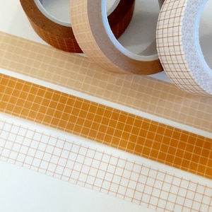 May include: Three rolls of washi tape with a grid pattern. The tape is beige, orange, and white with brown grid lines.