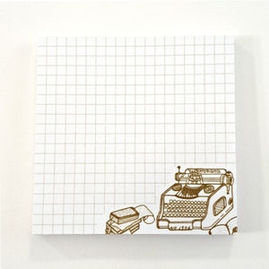 May include: A white notepad with a brown grid pattern. The notepad has a brown illustration of a vintage typewriter with a roll of paper and a stack of paper on the bottom right corner. The typewriter has the text "Yost Typewriter" and "No. 1906" on it.
