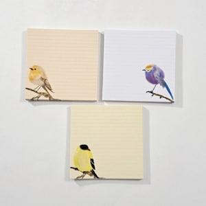 May include: Three lined notepads with different bird illustrations. The first notepad has a yellow bird with a brown head, the second notepad has a purple bird with a yellow head, and the third notepad has a yellow bird with a black head.