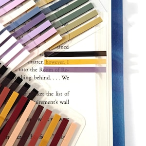 May include: A collection of colorful sticky page markers in various shades of purple, pink, yellow, green, and black. The markers are placed on a book with text visible. The text includes the words "matter, however. I" and "into the Room of Re-".