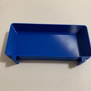 May include: A vibrant blue rectangular tray with a textured surface. The tray has a low profile with raised edges and small, rectangular supports on the sides. This item is likely a storage or organizational product.