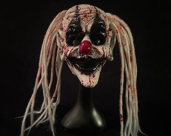 May include: A white creepy clown mask with red blood splatters and long white dreadlocks. The mask has a wide, toothy grin and a red clown nose.