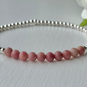 May include: A delicate bracelet featuring pink and silver beads. The bracelet is crafted with small, round silver beads and a row of larger, pink beads.