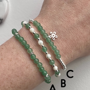 May include: Three green gemstone bracelets with silver beads and a silver charm. The bracelets are stacked on a person's wrist. The top bracelet has a silver flower charm. The bracelets are labelled A, B, and C.