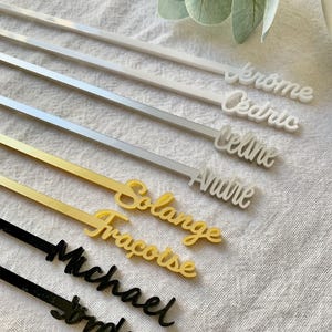 May include: A selection of personalised drink stirrers in white, silver, gold, and black. Each stirrer has a name in a cursive font. The names include Jerome, Cedric, Celine, Andre, Solange, Francoise, Michael, and Jordis.