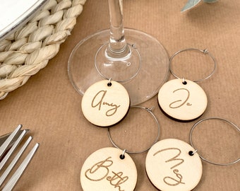 May include: Four wooden wine glass charms with names "Amy", "Beth", "Meg", and "Jo" engraved on them. The charms are attached to silver metal rings.