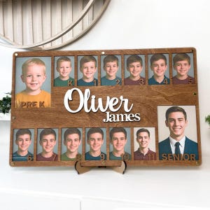 Peut inclure: Un présentoir photo en bois avec le nom "Oliver James" en écriture blanche. Il présente une série de photos scolaires de la maternelle à la dernière année, montrant la croissance d'une personne au fil du temps. Le présentoir est soutenu par un support en bois.