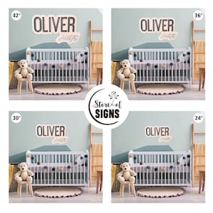 May include: A wall sign featuring the name Oliver Hunter in black and script lettering, displayed in four sizes: 42 inches, 36 inches, 30 inches, and 24 inches. The sign is shown mounted above a white crib with a teddy bear and a pom-pom garland.