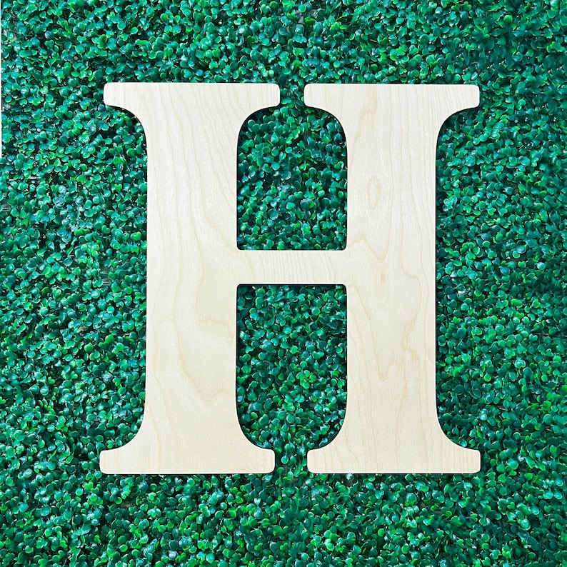 Op de afbeelding: Een grote, witte houten letter H, getoond tegen een achtergrond van groen kunstgras.