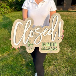 May include: A wooden sign with a light brown textured finish featuring the white 3D script text Closed! and the green 3D text by JAKARTA 678-313-4646. The sign has a layered, organic shape with rounded edges and a smooth, matte surface appearance.