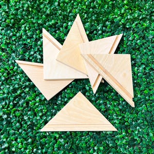 May include: A collection of wooden geometric shapes, including triangles and trapezoids, arranged on a green textured surface. The shapes have a natural wood grain and are designed with a groove detail.
