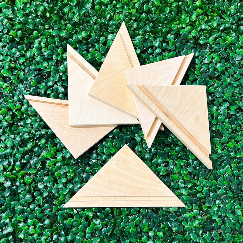 May include: A collection of wooden geometric shapes, including triangles and trapezoids, arranged on a green textured surface. The shapes have a natural wood grain and are designed with a groove detail.