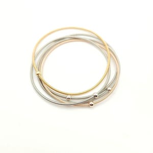 May include: Set of three gold, silver, and rose gold bangle bracelets with small ball accents.