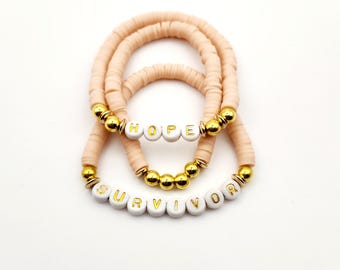 May include: Three beaded bracelets with the words "HOPE" and "SURVIVOR" spelled out in white beads with gold lettering. The bracelets are made with peach-coloured beads.
