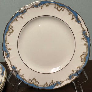 May include: A white porcelain plate with a blue and gold floral design. The plate has a scalloped edge and a gold rim.