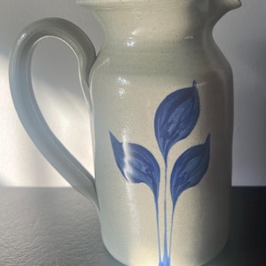 May include: A stoneware pitcher with a blue and white leaf design. The pitcher has a wide mouth and a handle.